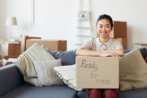 Portrait of young Asian woman holding cardboard box with ready to move inscription and smiling , copy space