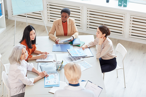High angle view at diverse group of successful businesswomen discussing project while sitting at table during meeting in modern white office, copy space