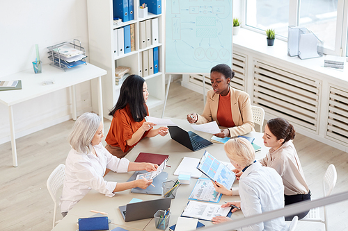 High angle view at multi-ethnic group of successful businesswomen discussing project while sitting at table during meeting in modern white office, copy space