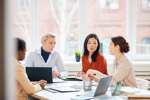 Portrait of diverse female business team discussing project while sitting at table during meeting in conference room against window, copy space