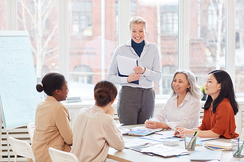 Portrait of successful female boss smiling happily looking at group of colleagues during meeting in modern white office, copy space