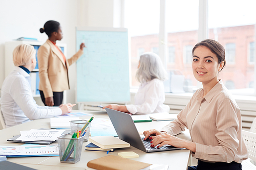 Portrait of elegant businesswoman smiling at camera while sitting at table in office during business meeting, copy space