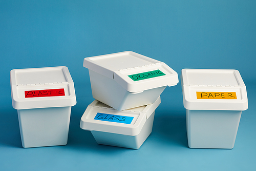 Labeled trash bins for plastic and paper waste in row against blue background, sorting and recycling concept, copy space