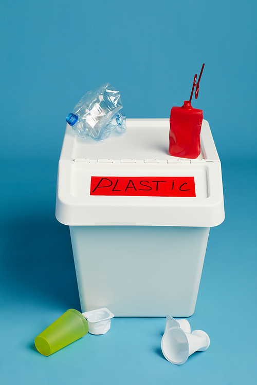 Full length view at labeled trash bin for plastic waste against blue background, sorting and recycling concept