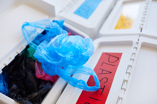 Close up of plastic bins labeled for storage and sorting waste at home, focus on discarded plastic bag in foreground, copy space