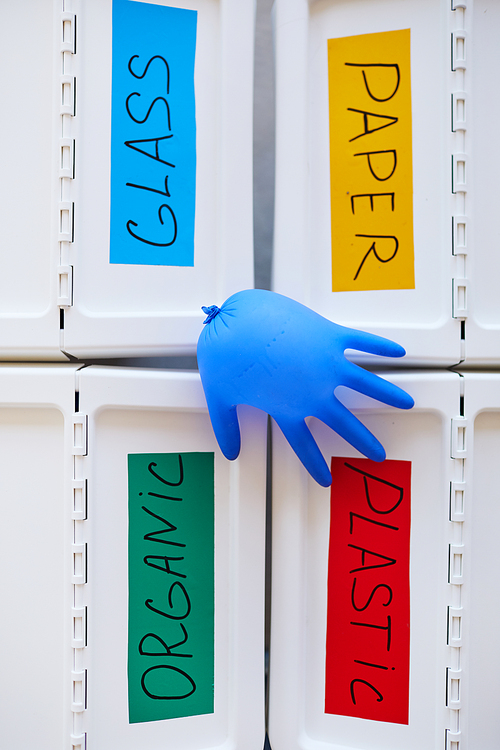 Above view background of four plastic bins labeled for storage and sorting waste at home, with blown rubber glove on top, copy space
