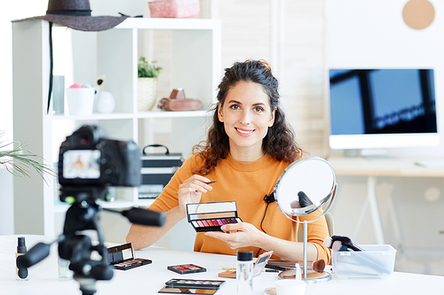 Horizontal portrait of young woman holding lipstick recording video for her beauty blog channel