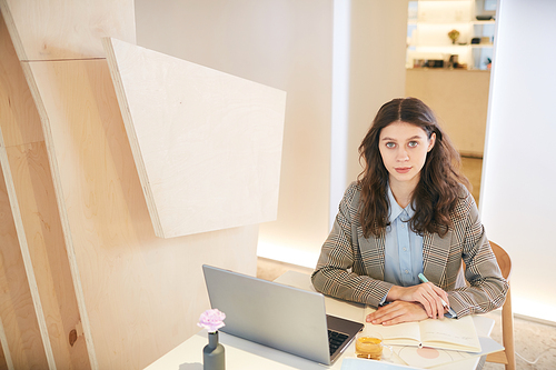 High angle portrait of pretty young woman working with laptop while sitting at desk in design interior, copy space