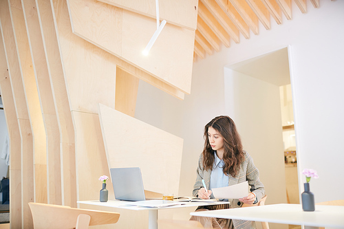 Wide angle portrait of pretty young woman working at desk in architectural design interior, copy space