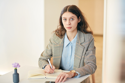 Portrait of pretty young woman  while taking notes sitting at white cafe table, copy space