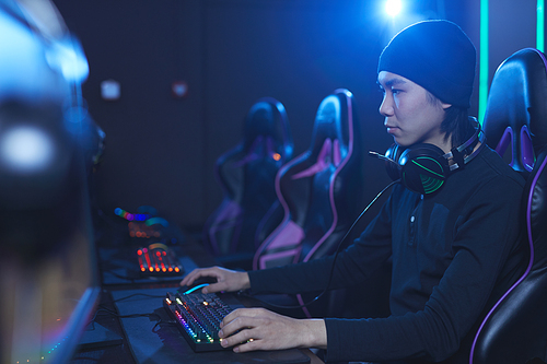 side view portrait of young asian man playing videogames in dark cyber  interior, copy space