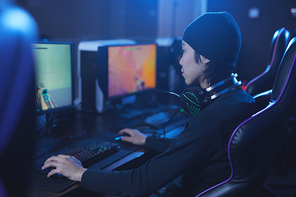 Back view portrait of Asian pro-gamer playing video games while sitting in dark cyber interior, copy space