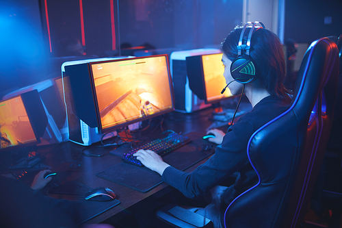 High angle view at young Asian man playing video games and wearing headphones in dark cyber sport interior, copy space