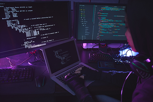 Unrecognizable young man surrounded by multiple screens programming or hacking security in dark room, copy space