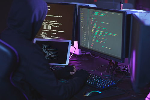 Back view of unrecognizable cyber security hacker wearing hood while working on programming code in dark room, copy space