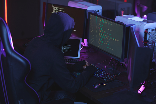 High angle view at unrecognizable cyber security hacker wearing hood while working on programming code in dark room, copy space
