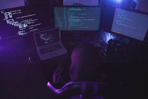 Top view at unrecognizable cyber security hacker wearing hood while working on programming code in dark room, copy space