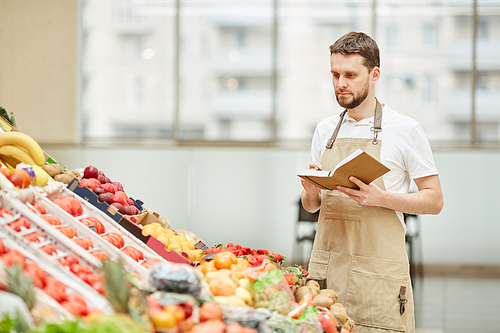 waist up portrait of bearded man wearing apron standing by fruit and  stand at farmers market while selling fresh produce, copy space