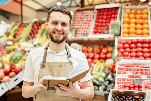 waist up portrait of bearded man wearing apron and smiling at camera while standing by fruit and  stand at farmers market, copy space