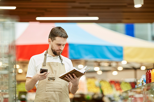 Waist up portrait of bearded man calling by smartphone while doing inventory count in supermarket, copy space