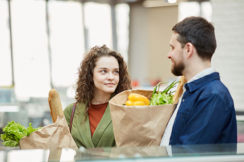 Waist up portrait of modern adult couple holding paper bags with groceries while enjoying shopping in supermarket, copy space