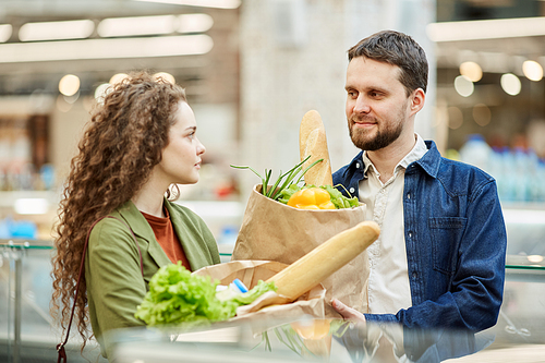 Waist up portrait of modern couple holding paper bags with groceries while enjoying shopping in supermarket, copy space