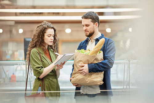 Waist up portrait of modern couple reading shopping list while buying groceries in supermarket, copy space