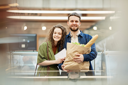 Waist up portrait of happy modern couple holding bag with groceries and  while enjoying shopping in supermarket, copy space
