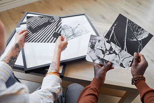 High angle close up of two modern young people discussing black and white pictures while choosing artwork for interior decor, copy space