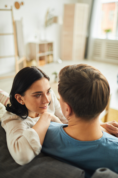 Warm toned high angle portrait of modern young couple looking at each other with love and affection while relaxing in home interior, copy space