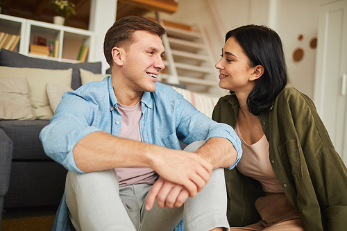 Warm toned portrait of modern young couple enjoying conversation while sitting on floor in cozy home interior, copy space