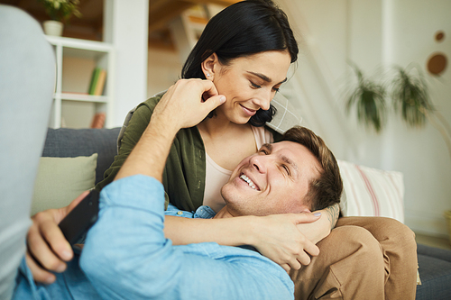Warm-toned portrait of carefree couple having fun at home while cuddling on sofa, copy space