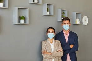 Minimal waist up portrait of confident business people wearing masks while standing with arms crossed against grey wall, copy space
