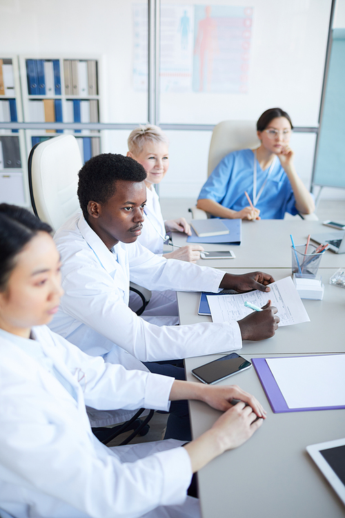 High angle view at young African-American doctor sitting at table during medical conference with colleagues, copy space