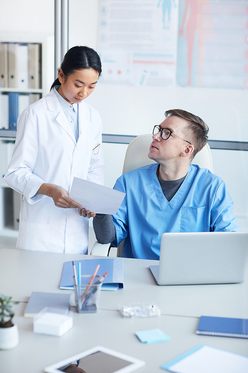 Vertical portrait of young Asian doctor consulting supervisor during internship in clinic, copy space