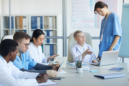 Group of doctors sitting round table during medical council or conference in clinic, copy space