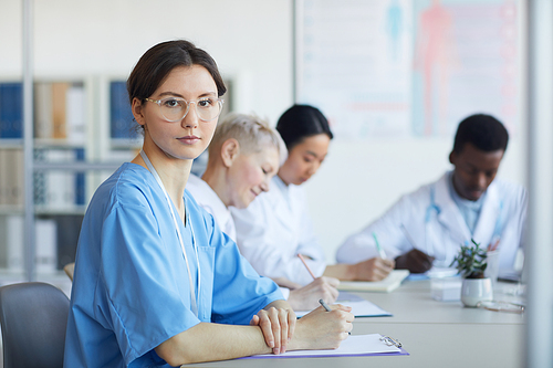 Portrait of young female doctor  while sitting at table during medical council or conference in clinic, copy space