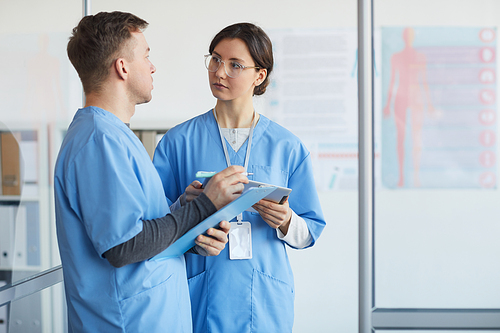 Waist up portrait of two medics holding clipboards while standing in medical office interior, copy space