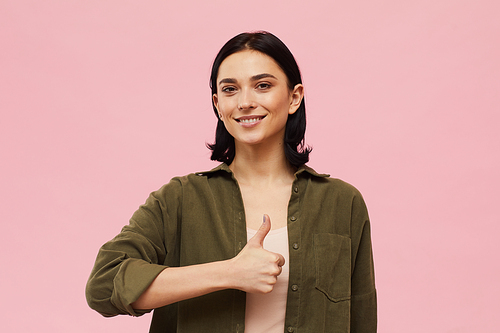 Waist up portrait of modern young woman showing thumbs up and  while standing against pink background in studio, copy space