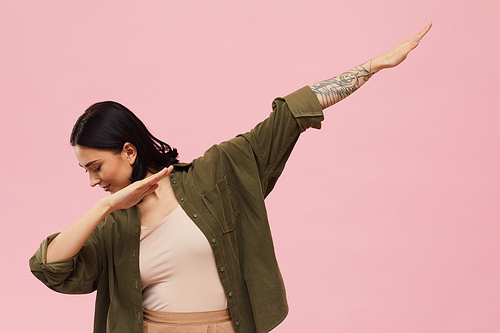 Waist up portrait of modern young woman dabbing while standing against pink background in studio, copy space