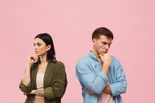 Waist up portrait of frustrated couple standing back to back against pink background, copy space