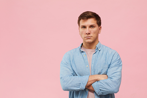 Waist up portrait of adult man standing with arms crossed and  while posing against pink background in studio, copy space