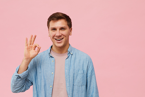 Waist up portrait of adult man showing OK sign and  while posing against pink background in studio, copy space