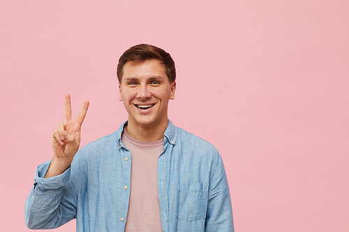 Waist up portrait of smiling man  while posing against pink background in studio, copy space