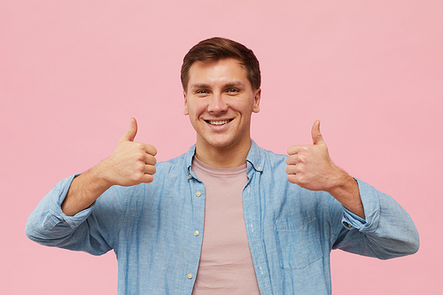 Waist up portrait of adult man showing thumbs up and  while posing against pink background in studio, copy space