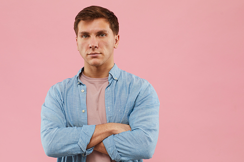 Waist up portrait of serious man standing with arms crossed and  while posing against pink background in studio, copy space