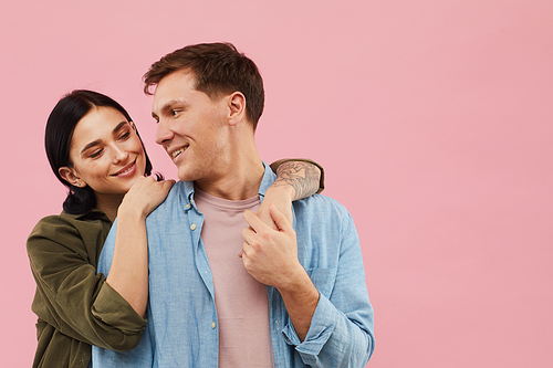 Waist up portrait of happy young couple posing against pink background in studio, copy space