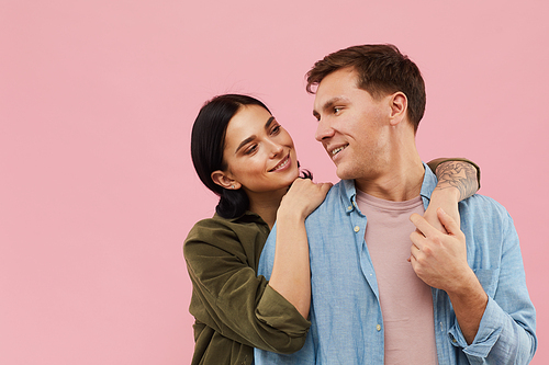 Waist up portrait of modern happy couple posing against pink background in studio, copy space