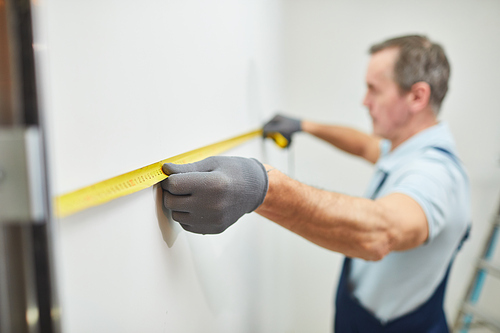 Closeup portrait of senior construction worker measuring wall while renovating house, copy space
