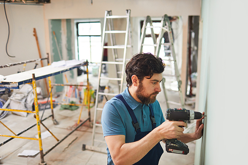 High angle portrait of bearded construction worker drilling wall while renovating house alone, copy space